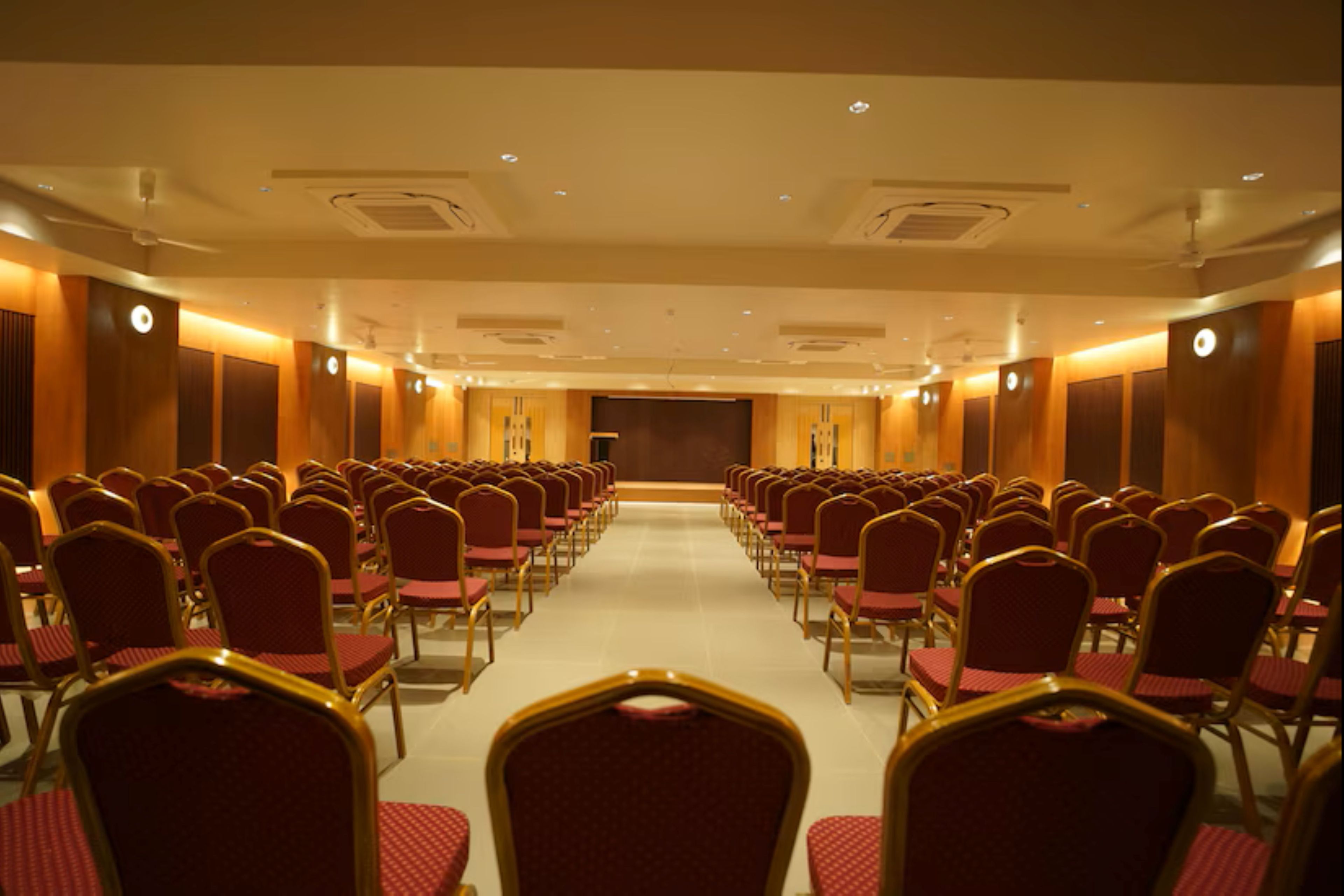 Un salón de conferencias con filas de sillas y un escenario al frente.