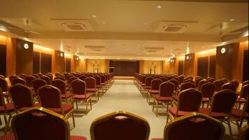 Un salón de conferencias con filas de sillas y un escenario al frente.