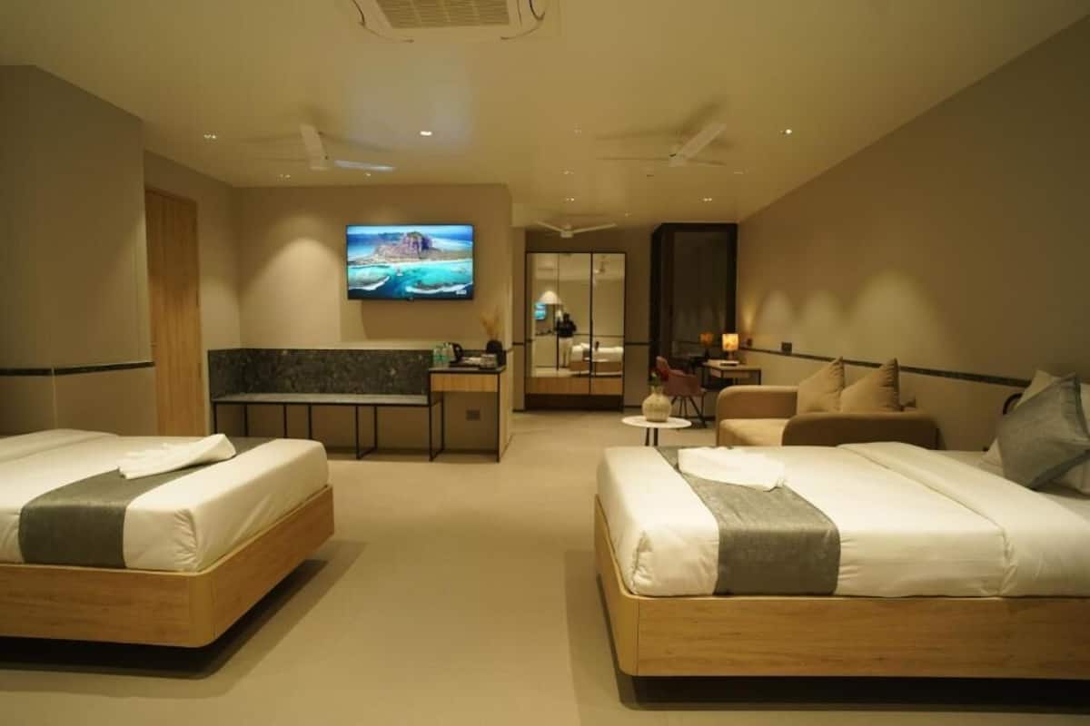 A hotel room with two beds, a desk, a TV, and a seating area.