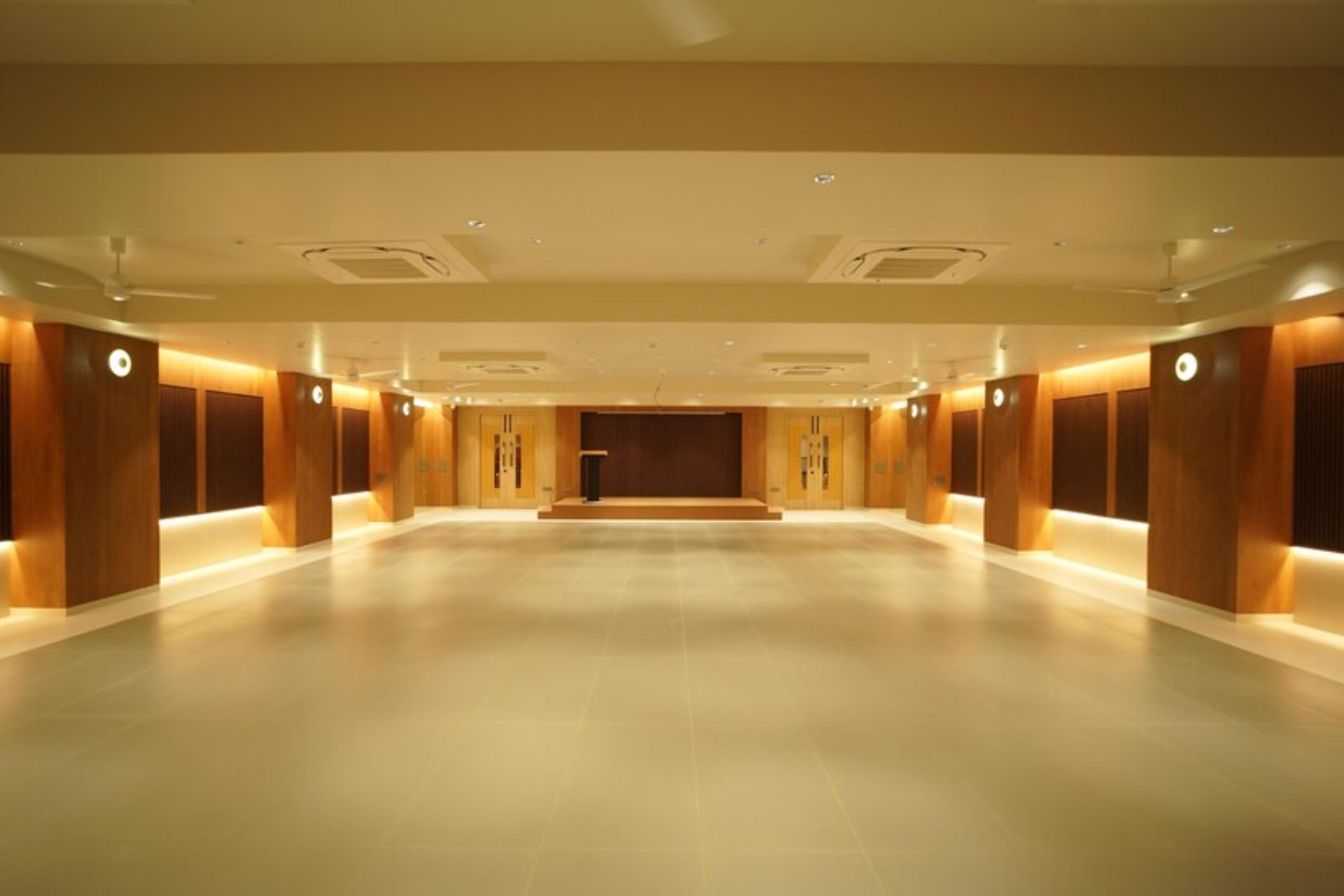 A spacious hotel lobby with a high ceiling, recessed lighting, and a central stage area.