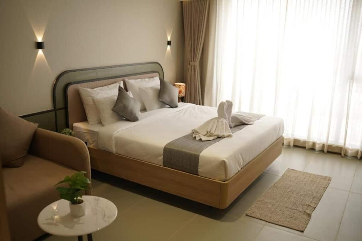 A hotel room with a bed, a sofa, a small table with a plant, and a window with curtains.