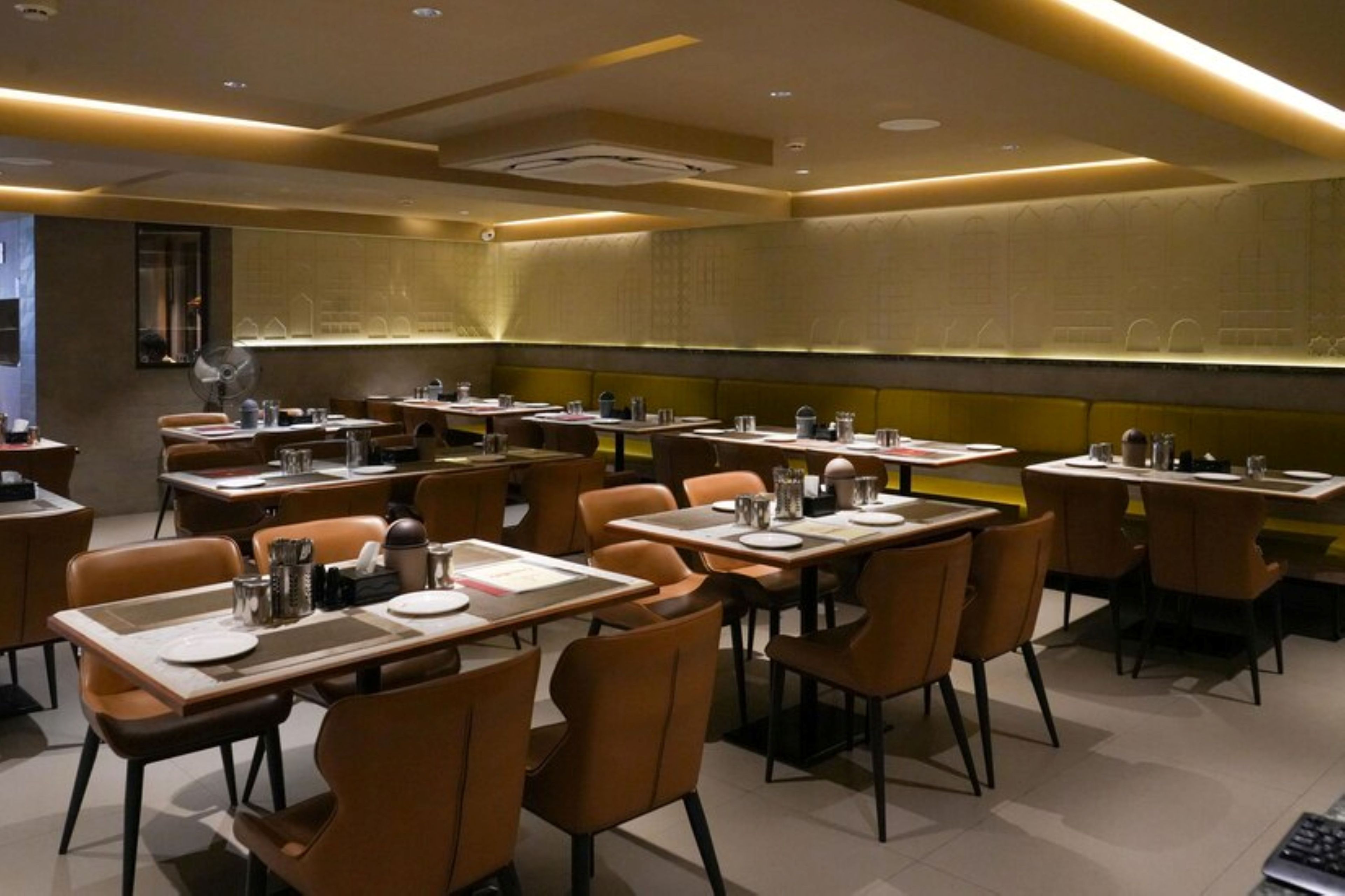 En restauranginteriör med flera bord och stolar, en modern takdesign och en vägg med ett diskret mönster.