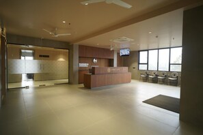 A reception area with a wooden reception desk, a clock, and a television screen. - HOTEL SANKET ELITE (Malegaon)
