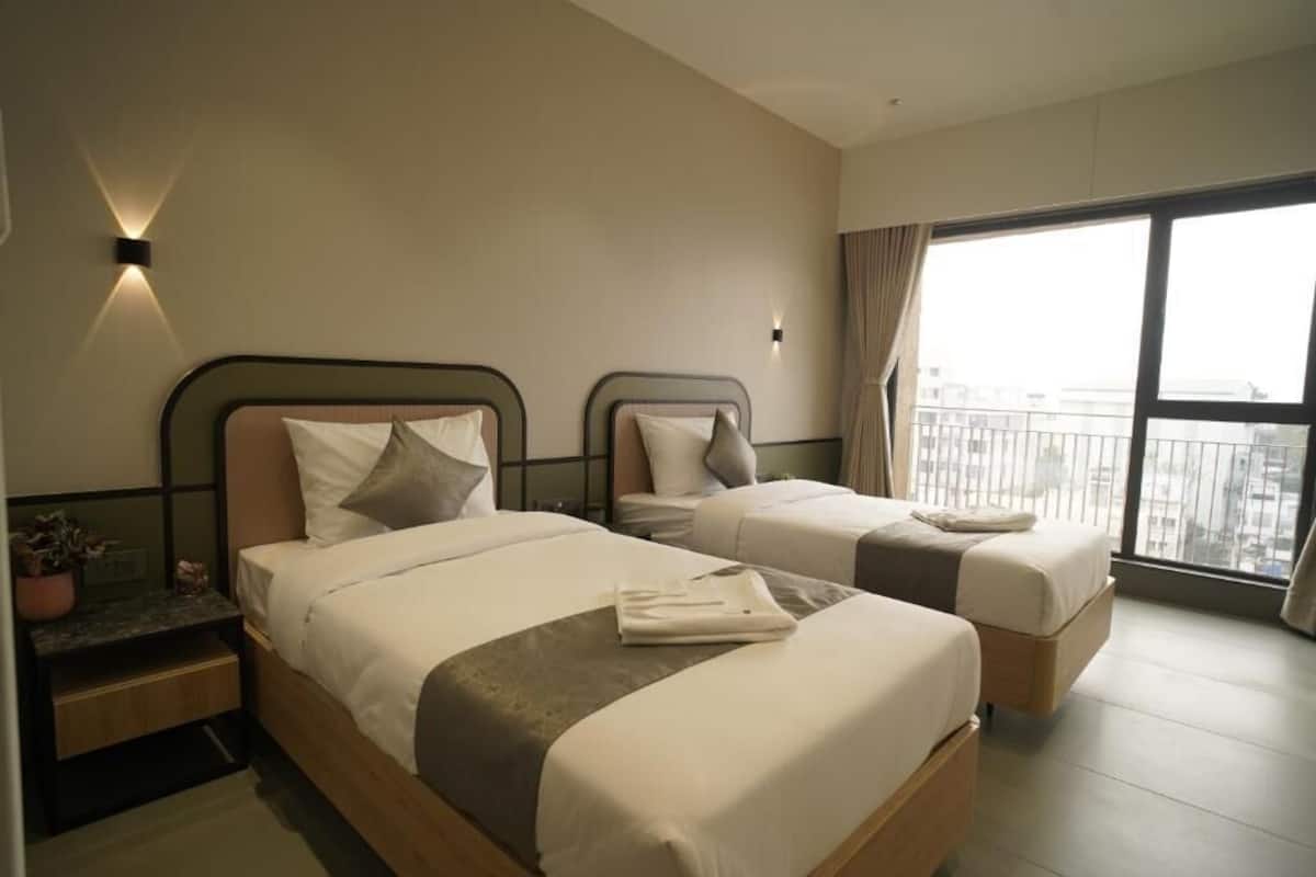 A hotel room with two beds, a nightstand with a plant, and a large window with a view.