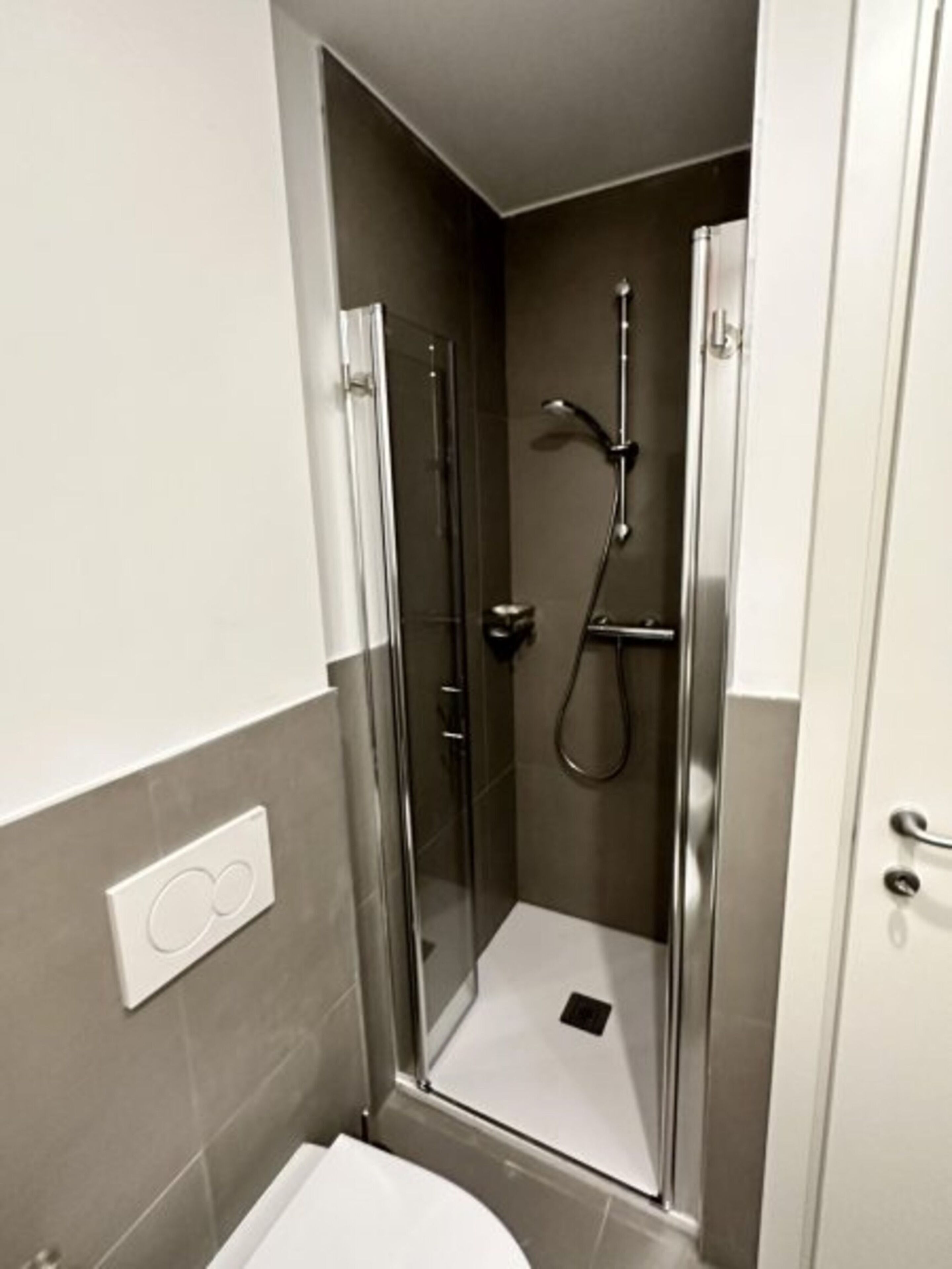 Une salle de bain moderne avec une douche à parois de verre, des toilettes et un interrupteur fixé au mur.