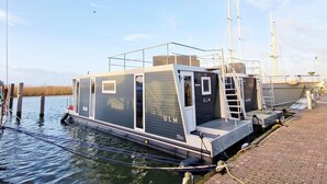 A modern floating structure with a dock, named 'ULM,' featuring a small deck and enclosed areas. - Floating Lodge With Terrace in Lelystad (Lelystad)