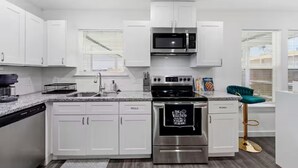 A modern kitchen with white cabinets, stainless steel appliances, and a bar stool. - Downtown Houston Modern Cozy Townhouse with Free Parking,WIFI and Near Airport (Houston)
