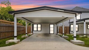 A covered garage with a concrete driveway, white siding, and black trim. - Downtown Houston Modern Cozy Townhouse with Free Parking,WIFI and Near Airport (Houston)
