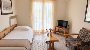 Una camera d'albergo con due letti, una TV su un mobile in legno, un divano a motivi decorativi e una finestra con tende leggere.
