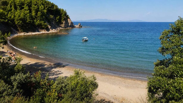 Une plage côtière aux eaux cristallines, avec un bateau et une végétation luxuriante.