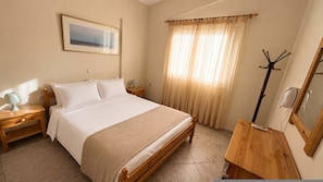 Un dormitorio con cama, mesitas de noche, un espejo, perchero y ventana con cortinas.