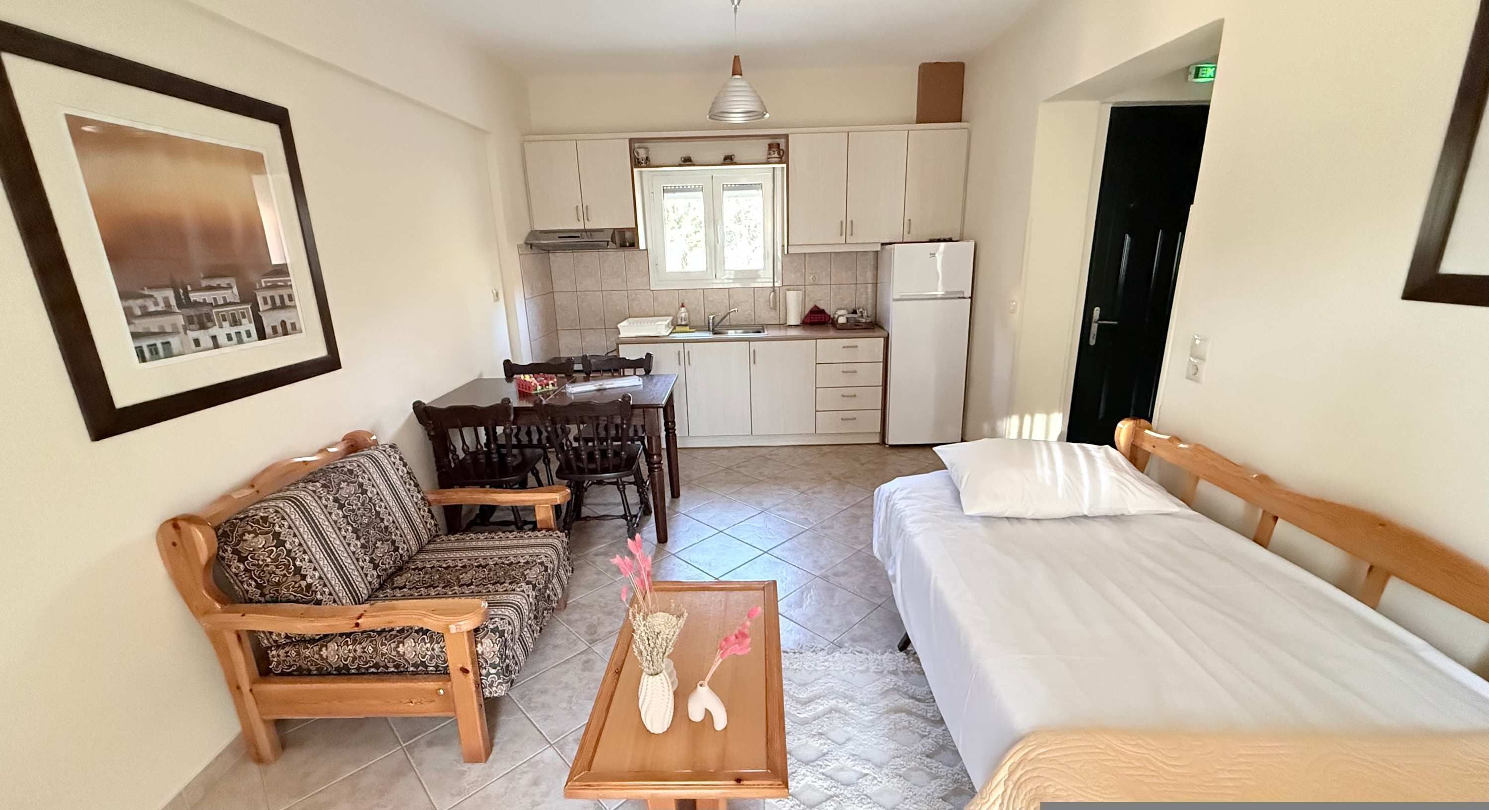 Quarto compacto com cama, sofá, mesinha, cozinha e quadro na parede.