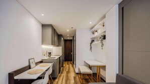 A narrow hallway with a kitchen area on the left, a dining table with chairs, and a small seating area with a bench on the right. - NOK Stylish Stay in Parque 93 (Bogotá)