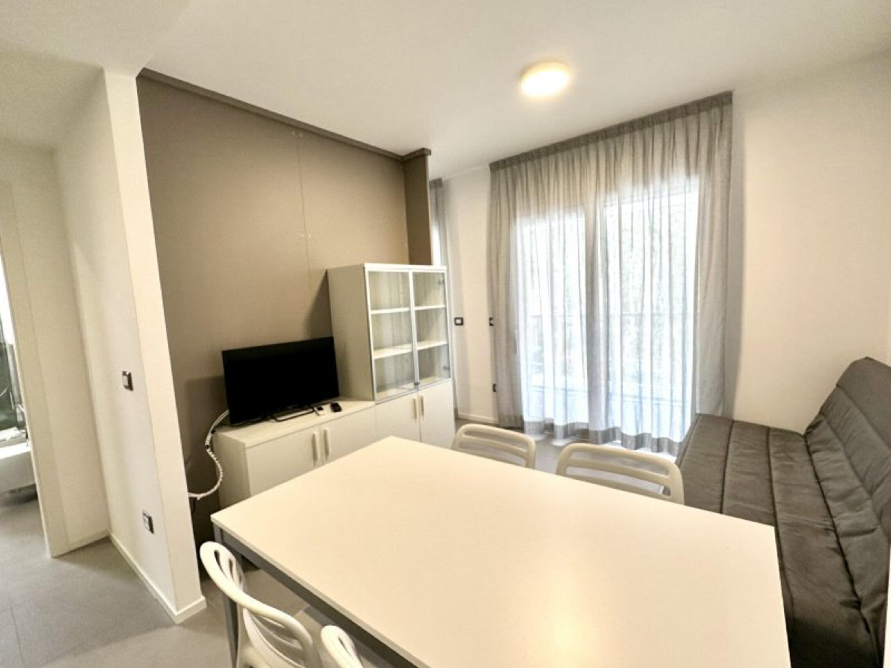 Una sala de estar moderna con un sofá, un televisor sobre un mueble bajo y un comedor con sillas.