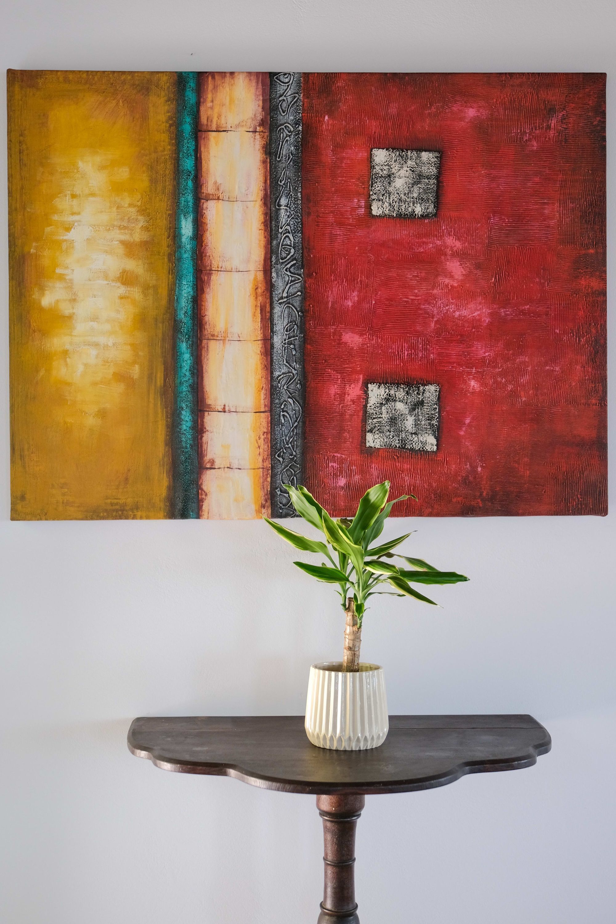 A painting with abstract patterns and a potted plant on a table.