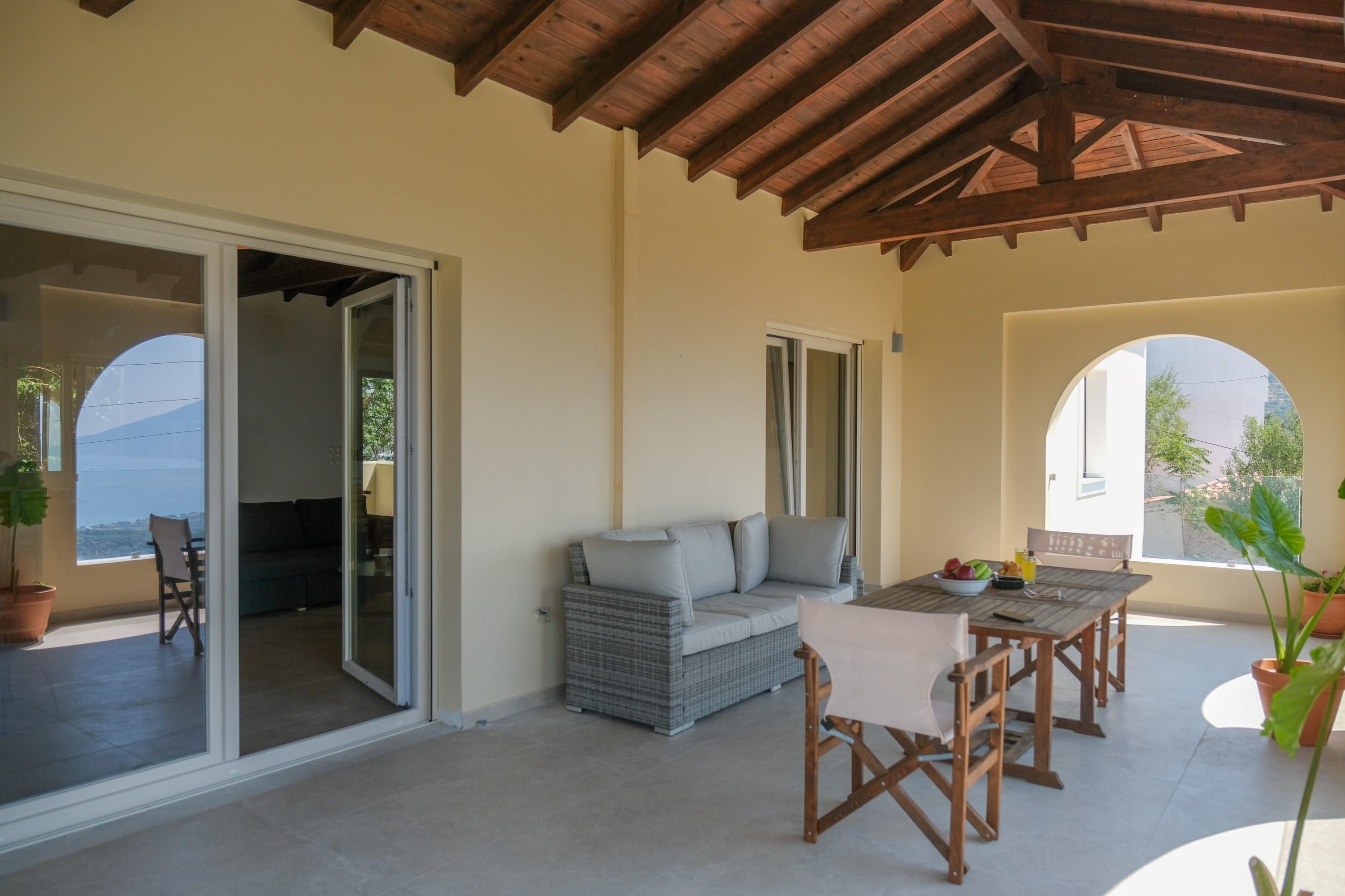 A covered patio with a dining table, chairs, a sofa, and a sliding glass door leading to an outdoor seating area.