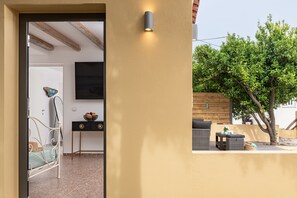 An interior room with a bed, a table with a bowl of fruit, and a wall-mounted TV. - Samos Sandy Angel - Seaside Garden Retreat (Samos)