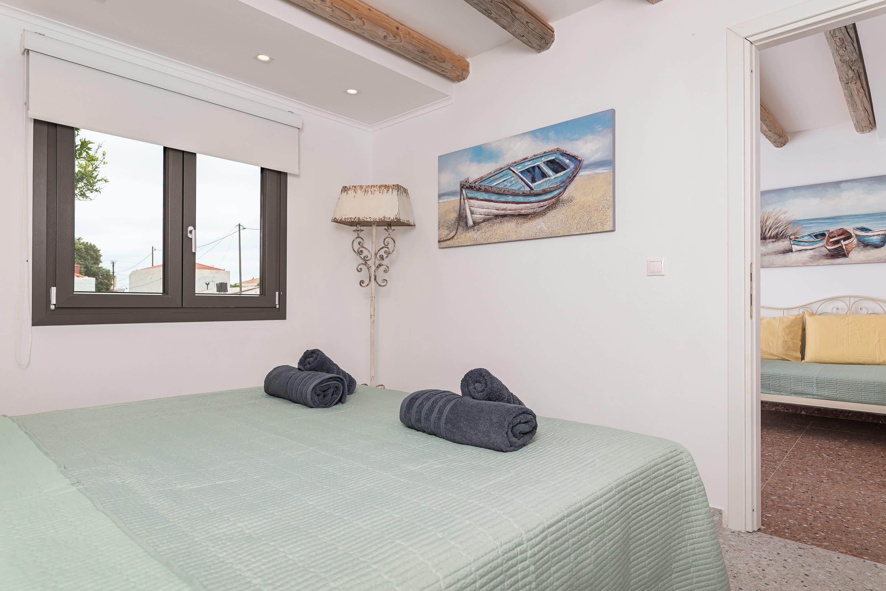 Ein Schlafzimmer mit Bett, Fenster, Lampe und zwei Bildern an der Wand.