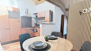 Une cuisine moderne avec des meubles en bois, un four à micro-ondes et une machine à café. On y trouve une table à manger avec des chaises et une petite plante.