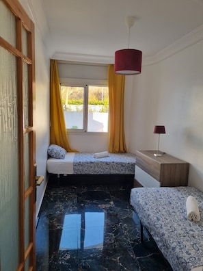 Ein Zimmer mit einem Bett, einem Nachttisch, einer Lampe, einem Fenster mit Vorhängen und einer Tür.