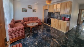 Eine moderne Küche mit Holzausstattung, einem Kühlschrank und einem Herd. Es gibt eine Sitzecke mit einer Couch und einem kleinen runden Tisch.