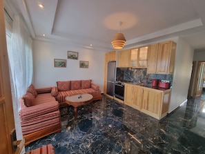 Eine moderne Küche mit Holzausstattung, einem Kühlschrank und einem Herd. Es gibt eine Sitzecke mit einer Couch und einem kleinen runden Tisch.