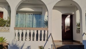 Ein Gebäude mit weißer Fassade, Bogenfenstern, einem Balkon mit Brüstung und einer Tür mit Metallbeschlägen.