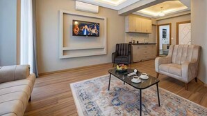 A modern living room with a sofa, a coffee table, a TV mounted on the wall, and a kitchen in the background. - Taksim Square - 1BR Deluxe Suite 101 (Istanbul)
