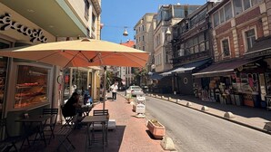 A street with outdoor seating, a sign for 'Papirus Hotel,' and various shops. - Taksim Square - 1BR Deluxe Suite 101 (Istanbul)