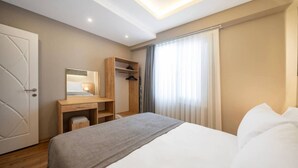 A hotel room with a bed, a desk with a mirror, a wardrobe, and a window with curtains. - Taksim Square - 1BR Deluxe Suite 101 (Istanbul)