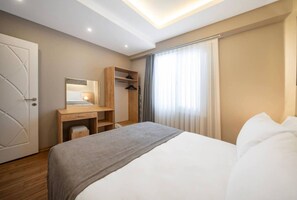 Ein Hotelzimmer mit Bett, Schreibtisch inklusive Spiegel, Kleiderschrank und einem Fenster mit Vorhängen.