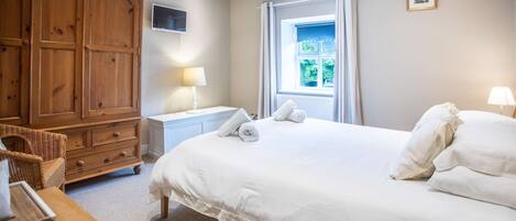 A bedroom with a large bed, wooden wardrobe, bedside tables, and a window with curtains.