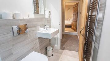 A modern bathroom with a white sink, mirror, and toilet. There is a wooden door leading to a bedroom.