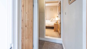 A hallway leading to a bedroom with a bed, bedside table, and lamp. - Cosy Stone Cottage In Gargrave Near Skipton (Skipton)
