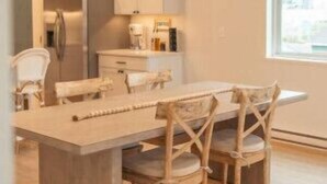 A modern kitchen with a central island, wooden chairs, and a hanging light fixture. - Park Point Lagom, Heirloom Vacations (Duluth)