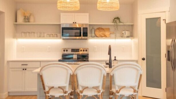 A modern kitchen with white cabinets, a microwave, an oven, and a dining area with three chairs. - Park Point Lagom, Heirloom Vacations (Duluth)