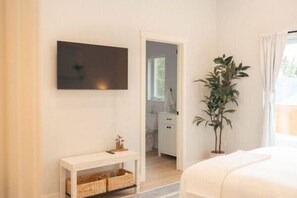 A bedroom with a bed, a TV mounted on the wall, a plant, and a doorway leading to another room. - Park Point Scandinavian Home, Heirloom Vacations (Duluth)