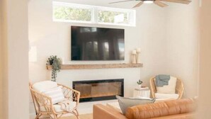 Ein Wohnzimmer mit Kamin, einem darüber montierten Fernseher und zwei Korbsesseln.