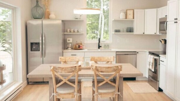 Eine moderne Küche mit weißen Schränken, einem Kühlschrank, einem Herd und einem Essbereich mit Holzkästen.