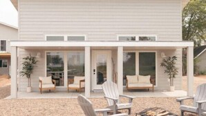 Ein modernes Haus mit überdachter Terrasse, weißen Außenwänden und einem Feuerkorb.