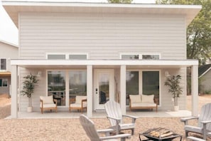 Ein modernes Haus mit überdachter Terrasse, weißen Außenwänden und einem Feuerkorb.