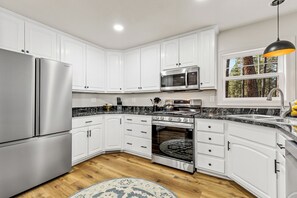 Una cocina moderna con armarios blancos, electrodomésticos de acero inoxidable, encimera de granito y suelo de madera.