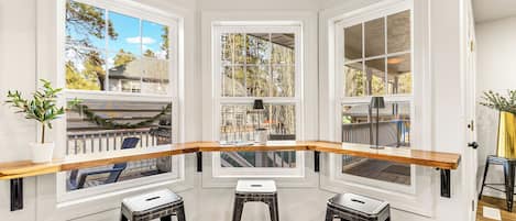Une cuisine d’angle avec trois fenêtres, un plan de travail en bois et deux tabourets.