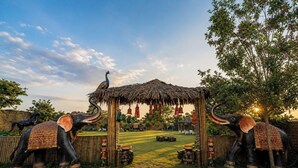 A thatched pavilion with hanging decorations, surrounded by elephant statues and a tree.