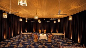 A room with a patterned carpet, a table with a white tablecloth, and several wicker chairs.