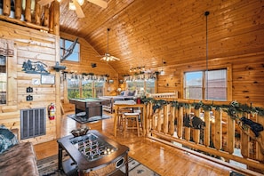 Ein Holzblockhaus-Interieur mit Billardtisch, Kamin und einer Terrasse mit Geländer.