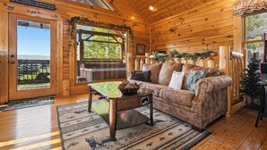 A wooden cabin interior with a couch, coffee table, and a view through the door. - We Love Dogs! Mountain Views, Hot Tub, WIFI, Pool Access, Free Attractions (Sevierville)