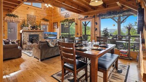 A cozy cabin interior with a fireplace, wooden furniture, and large windows offering a view of the outdoors. - We Love Dogs! Mountain Views, Hot Tub, WIFI, Pool Access, Free Attractions (Sevierville)