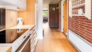A modern kitchen with a wooden countertop, a kettle, and a stove. There is a brick wall with a shelf holding glasses and a teapot. - 6 Person Holiday Home in Norre Nebel (Norre Nebel)