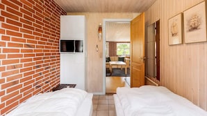 A room with two beds, a TV mounted on a brick wall, and wooden paneling. - 6 Person Holiday Home in Norre Nebel (Norre Nebel)